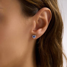 Close-up of an ear wearing a heart-shaped blue earring with a white center.