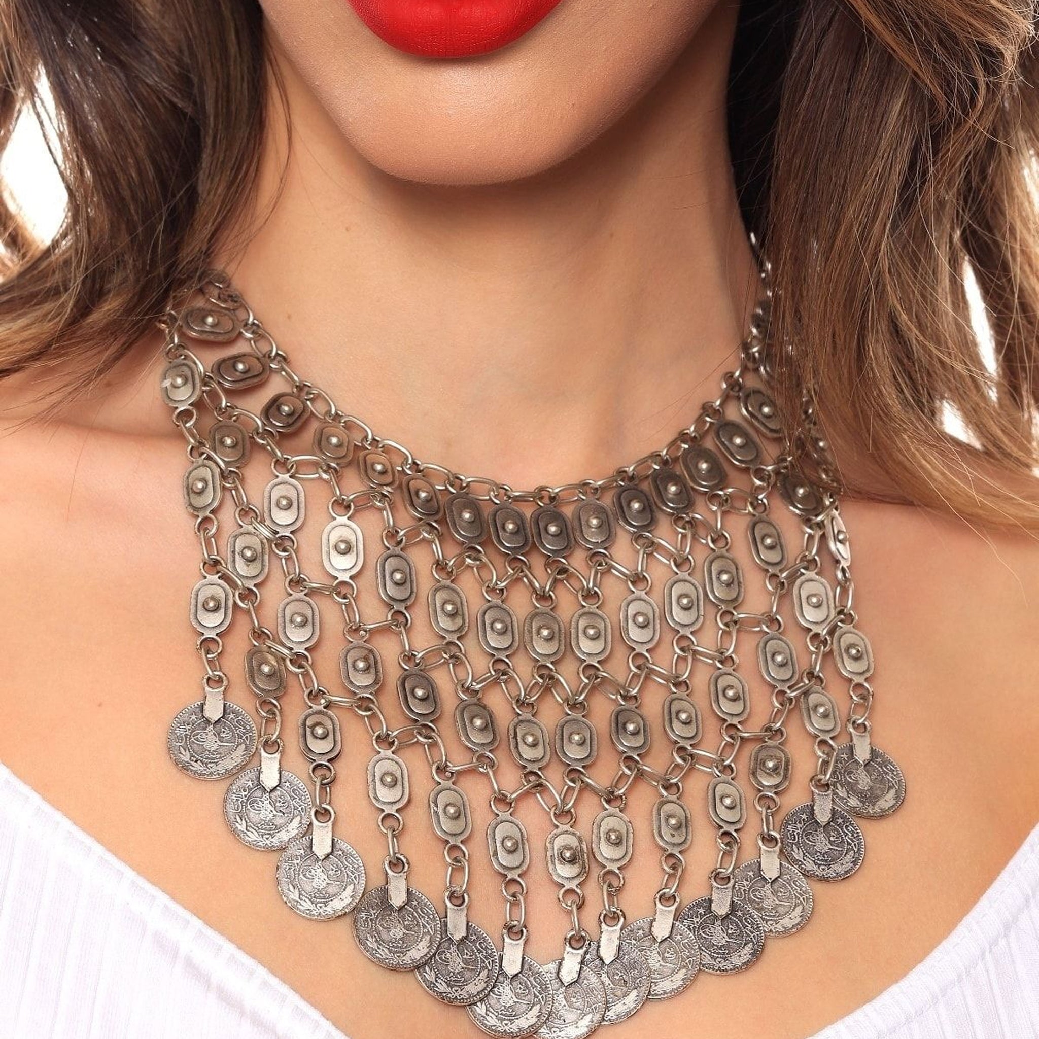 Silver necklace with coin pendants worn by a person with red lipstick.