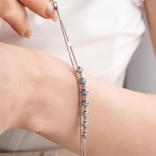 Close-up of a hand wearing a bracelet with blue stones on a neutral background