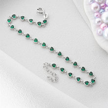 Silver bracelet with green heart-shaped beads on a white surface