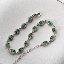 Silver bracelet with green gemstones on a white background