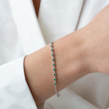 Silver bracelet with green beads on a wrist against a white background