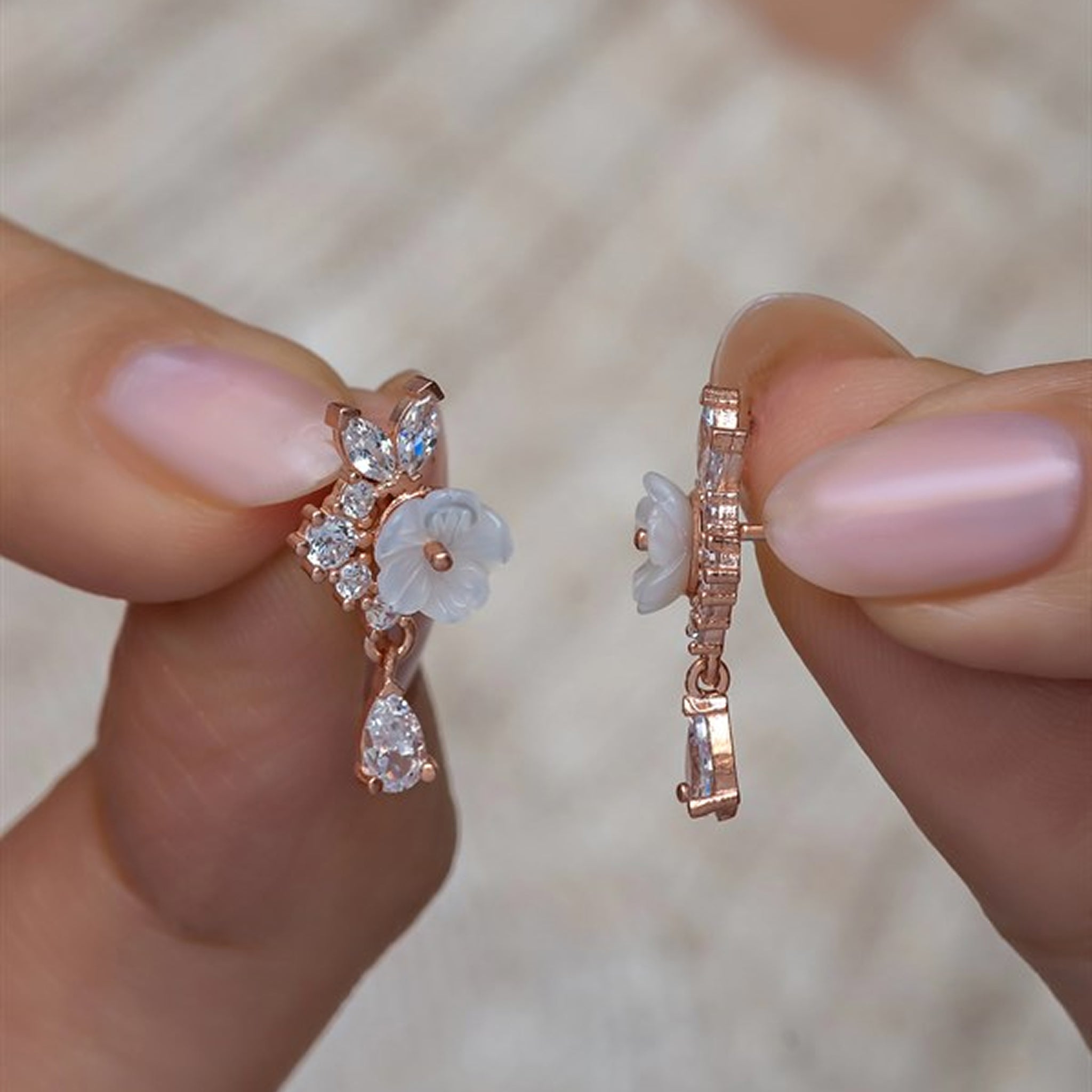 Rose gold earrings with floral design held between fingers against a blurred background