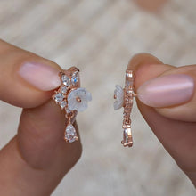 Rose gold earrings with floral design held between fingers against a blurred background