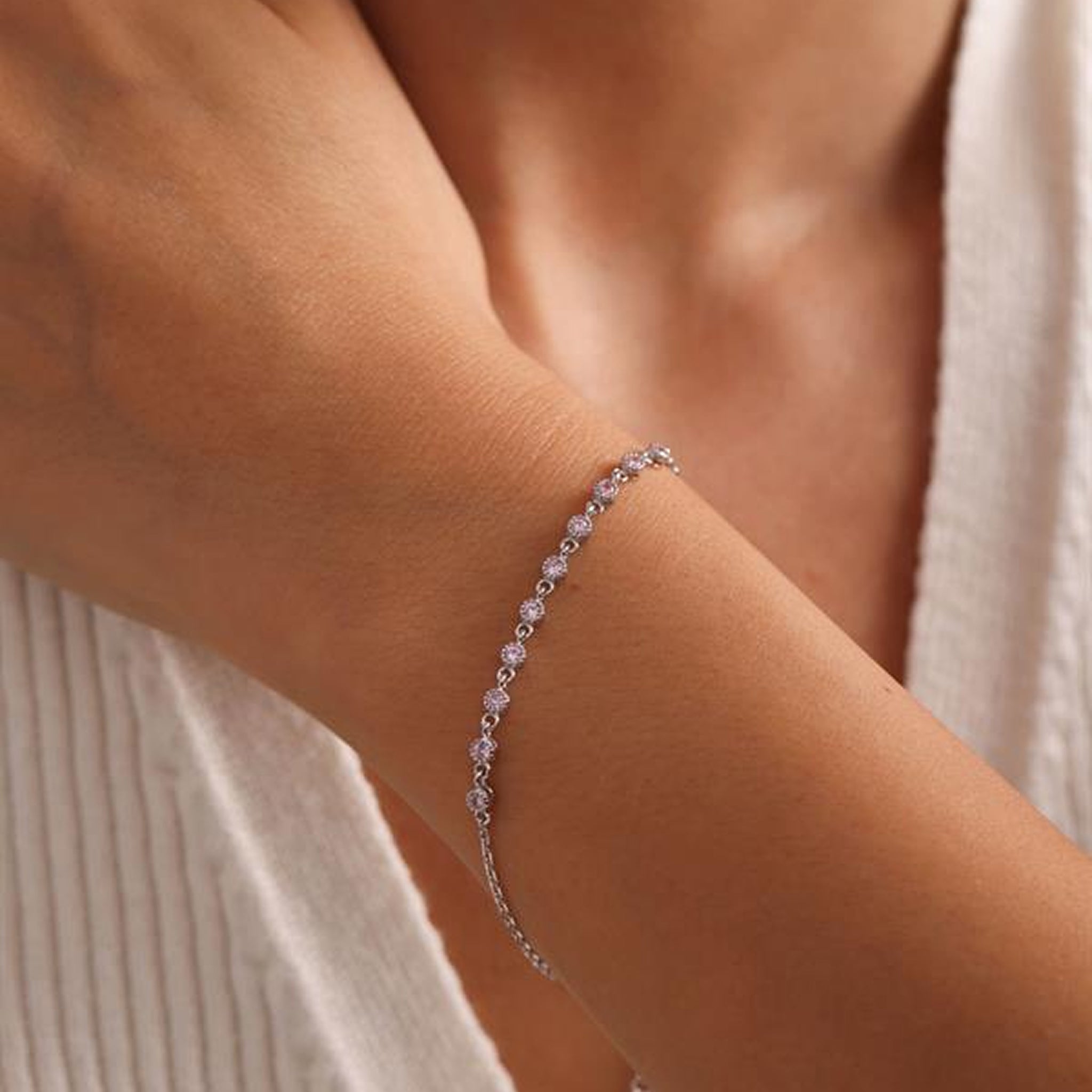 Silver bracelet with small stones on a person's wrist against a neutral background