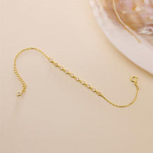 Gold chain bracelet on a beige surface with a shell in the background