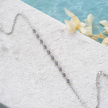 Silver necklace with purple stones on a white surface with a blurred background