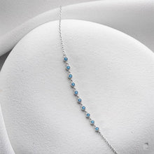 Delicate silver bracelet with blue stones on a white jewelry display.