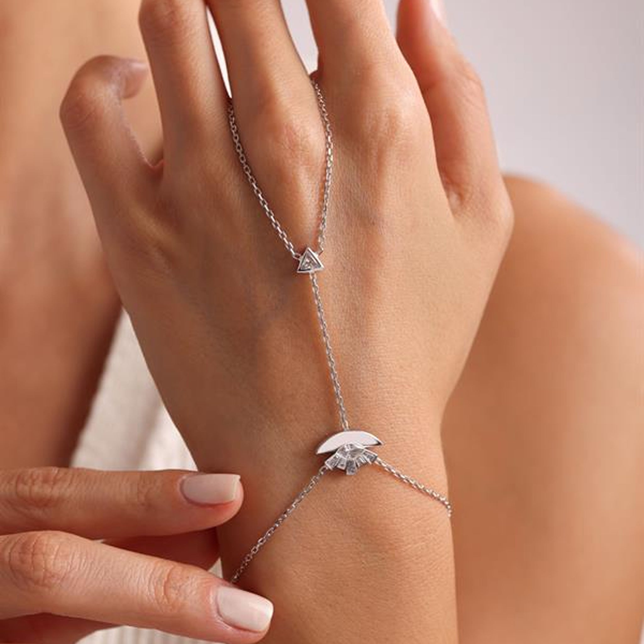 Silver bracelet with a triangle-shaped charm on a wrist against a neutral background