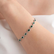 Silver bracelet with green gemstones on a wrist against a light background