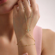 Gold hand chain with eye design on a hand against a blurred background