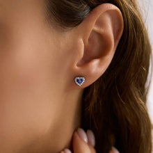 Close-up of an ear wearing a heart-shaped earring with blue and purple stones.