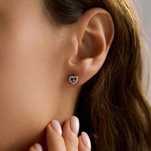 Close-up of an ear wearing a heart-shaped earring with a blue stone.