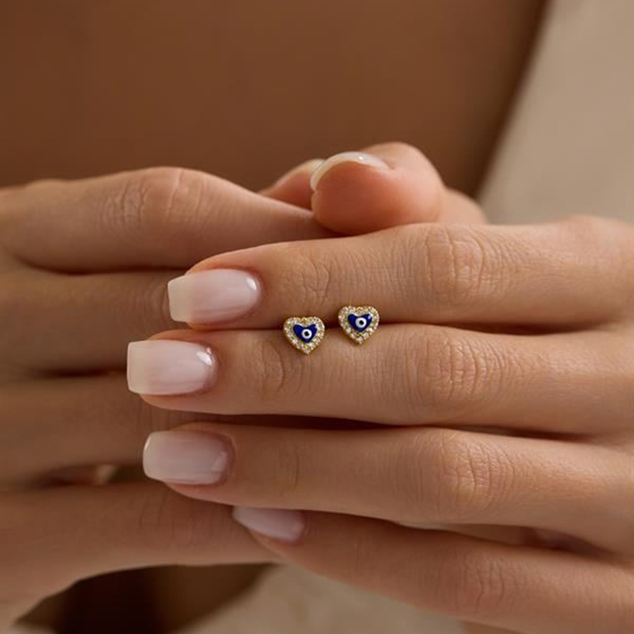 Heart-shaped earrings with blue and gold accents held between fingers against a neutral background
