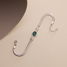 Silver bracelet with a green gemstone on a beige background