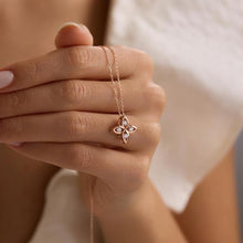 Rose gold necklace with a floral pendant held by a hand against a neutral background