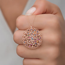 Rose gold necklace with a colorful pendant held in a hand against a neutral background
