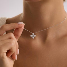 Silver necklace with a floral pendant held by a hand against a neutral background