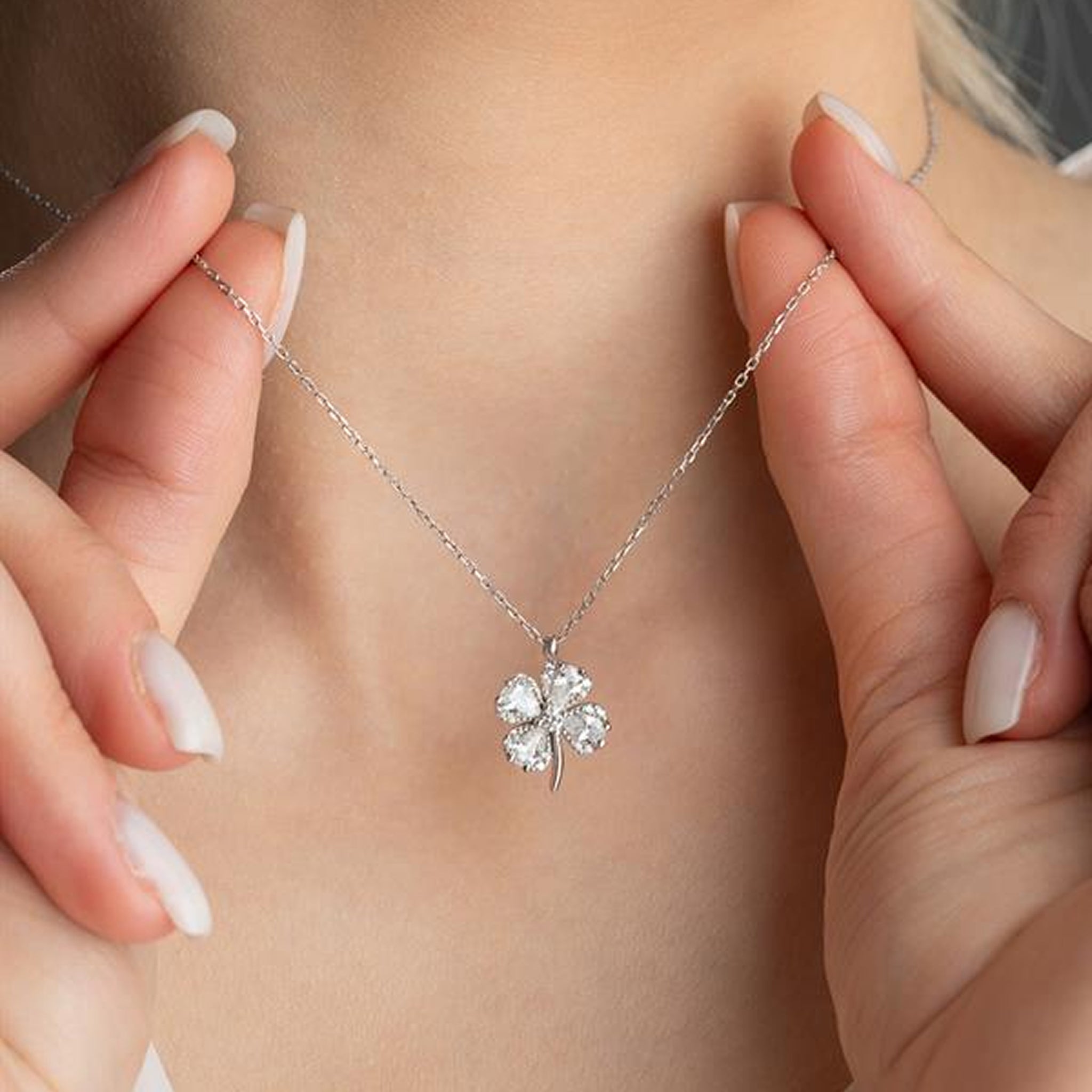 Silver necklace with a clover-shaped pendant held by hands against a neutral background