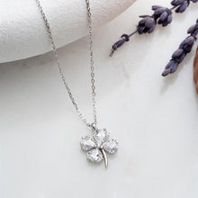 Silver four-leaf clover necklace on a white surface with lavender flowers.