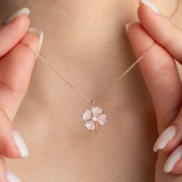 Rose gold necklace with a floral pendant held by hands against a neutral background