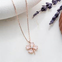 Rose gold necklace with a pink clover pendant on a white surface with lavender.