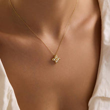 Gold necklace with a floral pendant on a person wearing a white shirt.