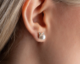 Pearl earring with cat-shaped design worn on an ear