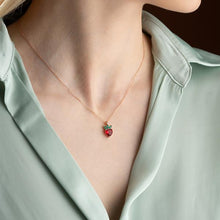 Necklace with a strawberry pendant worn by a person in a light green shirt.