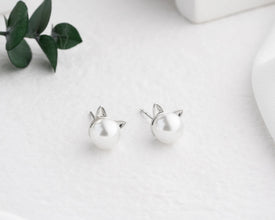 Silver cat-shaped earrings on a light gray background with green leaves.