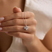 Silver necklace with a floral pendant held by a hand against a neutral background