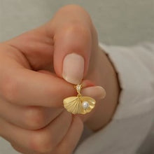 Gold earring with a pearl pendant held by a hand against a neutral background