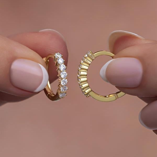 Gold hoop earrings held between fingers against a blurred background