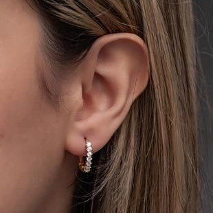 Close-up of an ear wearing a small hoop earring with clear stones.
