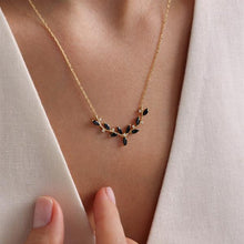Gold necklace with black stones worn by a person against a neutral background