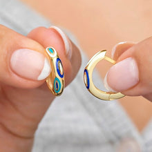 Gold hoop earrings with blue and green accents held between fingers against a neutral background