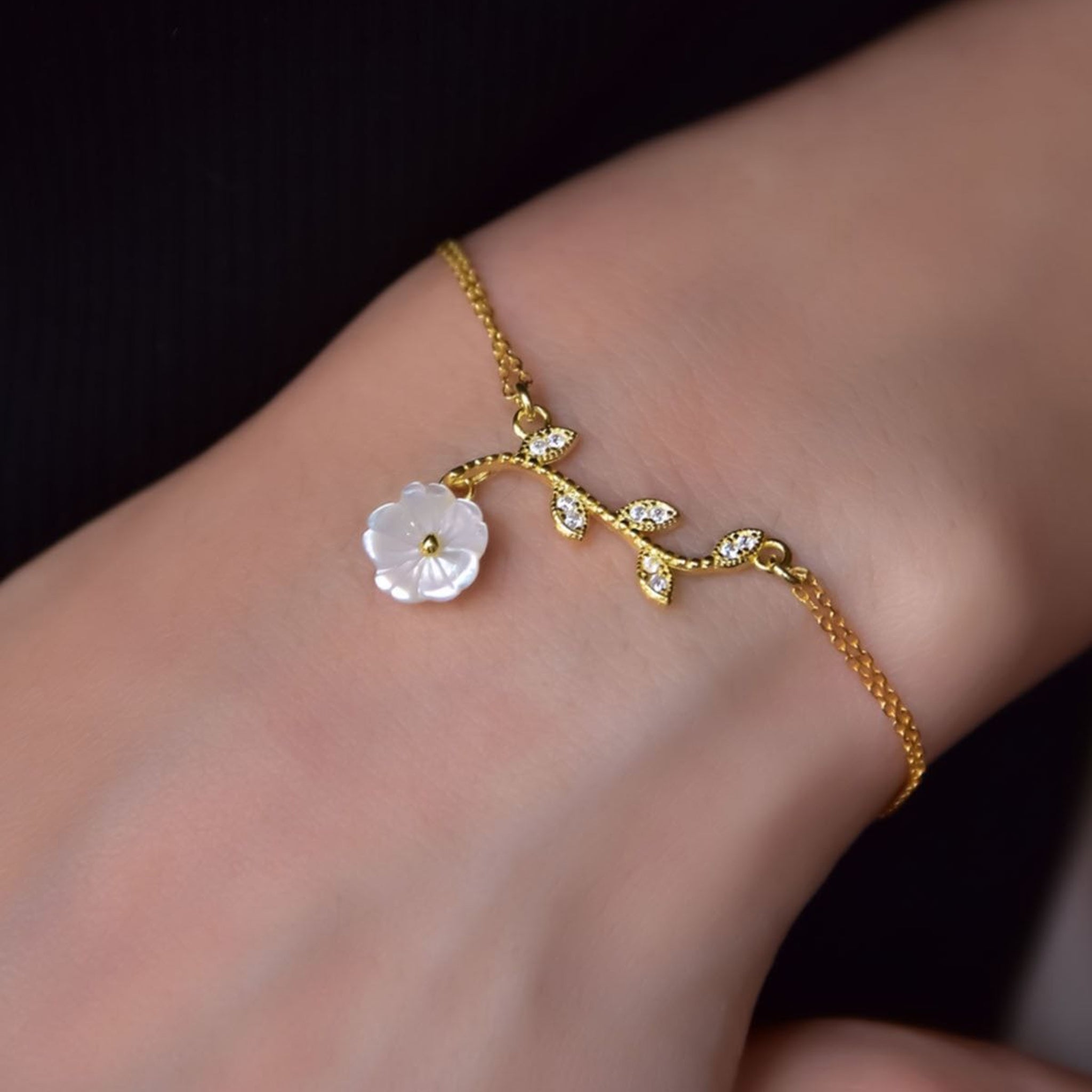 Gold anklet with a white floral charm on a wrist against a dark background