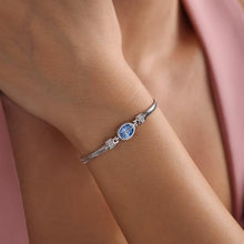 Silver bracelet with a blue gemstone on a wrist against a pink fabric background