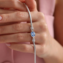 Silver bracelet with a blue gemstone held by a hand against a pink background