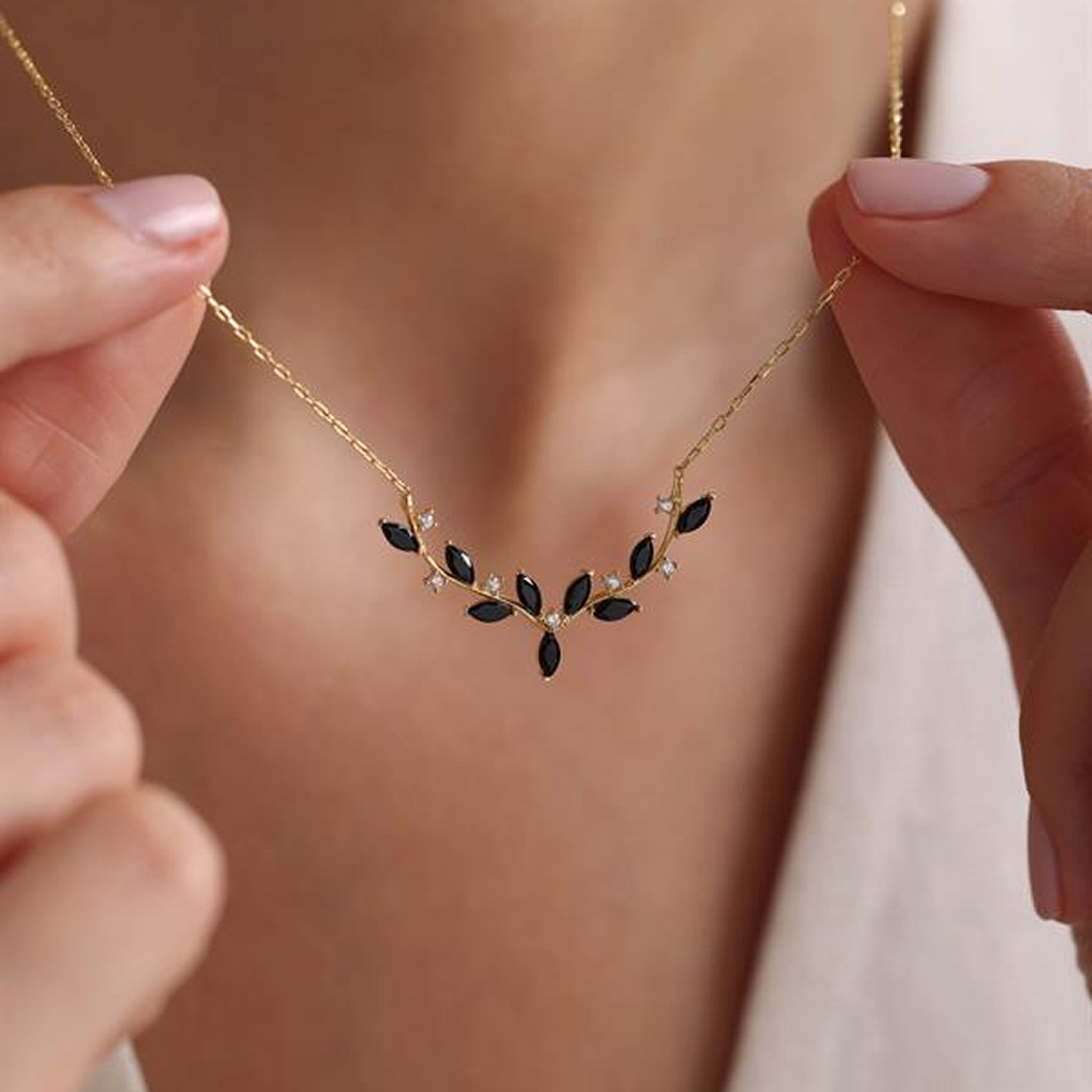 Gold necklace with black and white gemstones held by hands against a blurred background