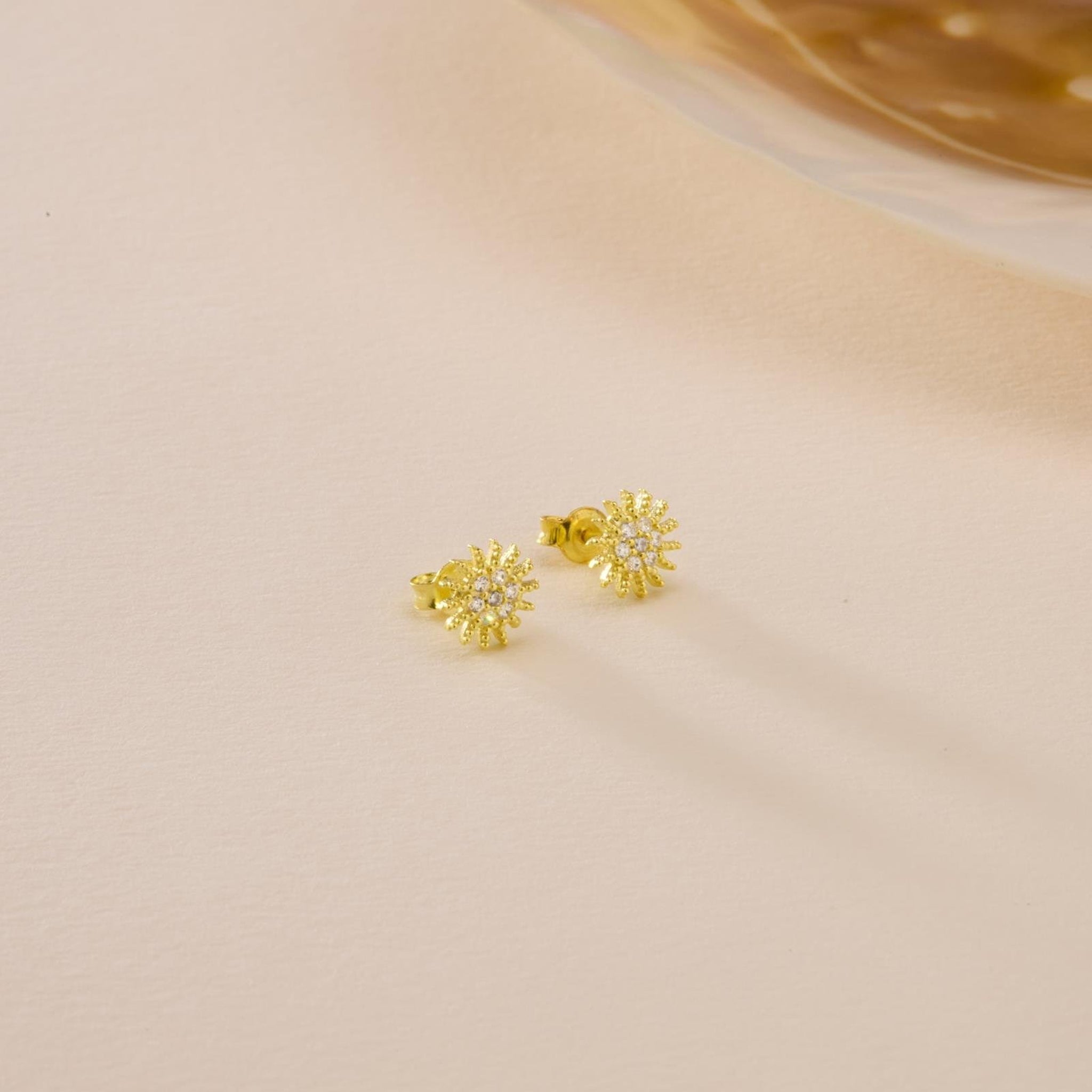Gold snowflake earrings on a beige background