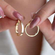 Gold hoop earrings held between fingers with a neutral background
