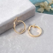 Gold hoop earrings on a textured surface with a soft background