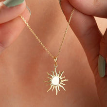 Gold sun-shaped pendant necklace on a chain held by a hand.