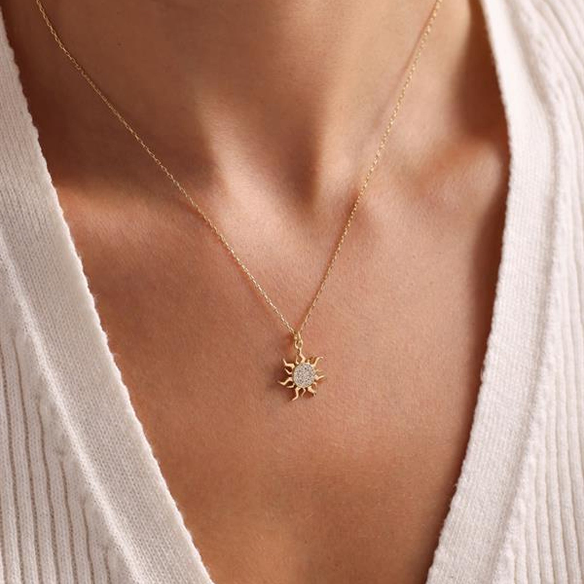 Gold necklace with a sun pendant worn by a person in a white cardigan.