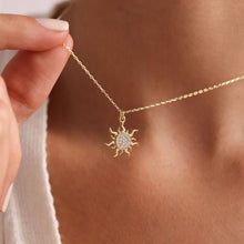 Gold necklace with sun pendant held by a hand against a neutral background