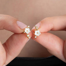 Flower-shaped earrings held between fingers against a neutral background