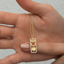 Gold necklace with a pendant held in a hand against a neutral background