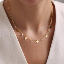 Gold necklace with round pendants on a person wearing a beige top.