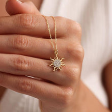 Gold sun-shaped necklace with clear stones held by a hand against a neutral background